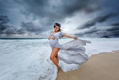 a woman in a white dress is running on the beach with her long flowing fabric