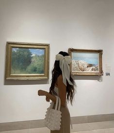 a woman looking at two paintings on display in an art gallery with one holding a purse