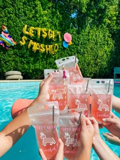 several people holding up plastic cups in front of a swimming pool