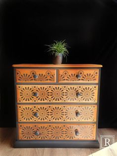 a wooden dresser with an ornate design on the front and drawers, has a potted plant on top