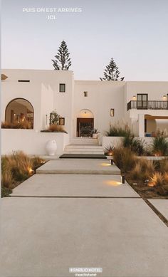 a large white house with lots of plants and lights on the front door, along with steps leading up to it