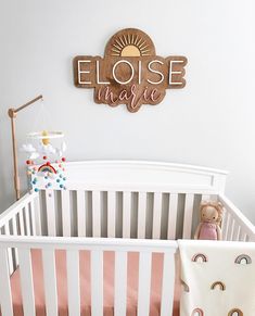 a white crib with a teddy bear in it and a wooden sign above the crib