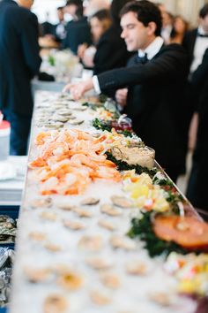 people are standing at a buffet table with food on it