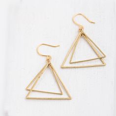 "A fun pair of double triangle earrings. The earrings are made with of triangles that fit into each other and dangle from gold plated ear wires. The bigger triangle measures 1\", the smaller 0.75\". DETAILS Double Triangle Earrings Hanging height from top of ear wires 1.75\" Drop length 1\" Made of brass Ear wires are gold plated Handmade by Nest Pretty Things Shipped in a gift box." Triangle Gold Metal Earrings, Gold Triangle Metal Earrings, Gold Triangle Minimalist Earrings, Minimalist Gold Triangle Earrings, Minimalist Triangle Nickel-free Earrings, Gold Triangle Jewelry With Ear Wire, Minimalist Nickel-free Triangle Earrings, Everyday Gold Triangle Earrings, Minimalist Triangle Hoop Earrings As Gift