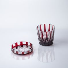 a red and white striped glass bowl next to a clear glass cup on a reflective surface