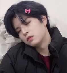 a young man with black hair wearing a pink bow clip on his head and sleeping