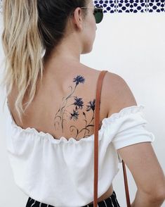 the back of a woman's shoulder with flowers tattooed on her left arm and behind her is a brown purse