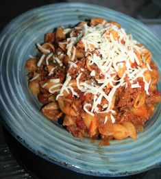 a blue plate topped with pasta and meat covered in cheese on top of it's side