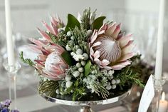 an arrangement of flowers and greenery in a silver bowl on a dining room table