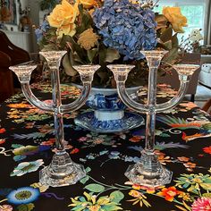 three glass candlesticks sitting on top of a table covered in colorful flowers and foliage