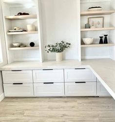 a kitchen with white cabinets and shelves filled with pots, bowls and vases on top of them