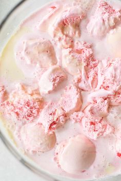 a glass bowl filled with ice cream and pink colored powdered doughnuts, on top of a white surface