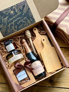 an open gift box containing two bottles of wine, cheese and jam with a wooden cutting board