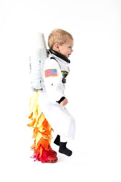 a little boy dressed in an astronaut suit and holding a rocket on top of his back