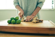 a woman is cutting up some vegetables on a wooden table with limes and ginger