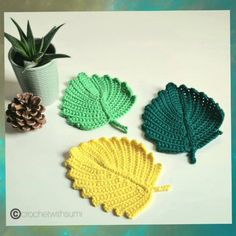 four crocheted leaves are shown next to a potted plant and pine cone