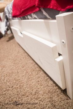 a white bed frame sitting on top of a carpeted floor next to a red pillow