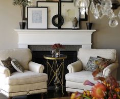 two white chairs sitting next to each other in front of a fire place with pictures on the wall