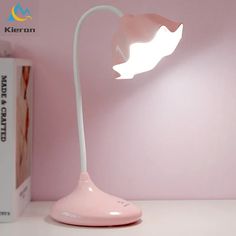 a pink desk lamp sitting on top of a white table next to a bookcase