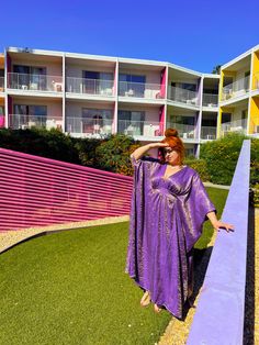 a woman standing on the grass in front of an apartment building with pink and yellow walls