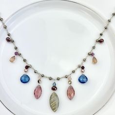 Elegant drape necklace featuring Marquee Gems as accents on Pyrite rosary style chain with draping marquee Labradorite and Marsala Qz, heart shape Spinel Qz and teardrop Dk Tea Qz. Length: 18-20″ (can request up to 24″ as well, no extra charge) Best Selling Necklace! Silver Drop Necklace With Gemstone Accents, Teardrop Gemstone Accents Necklace For Jewelry Making, Bohemian Silver Briolette Necklaces, Silver Teardrop Crystal Necklace With Faceted Beads, Silver Drop Necklaces With Faceted Beads, Silver Teardrop Necklace With Faceted Beads, Teardrop Stones For Jewelry Making Necklaces, Silver Teardrop Gemstone Beaded Necklace, Silver Teardrop Necklace With Gemstone Beads