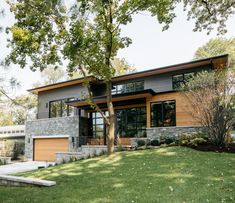 a modern house with stone and wood sidings on the front, surrounded by green grass