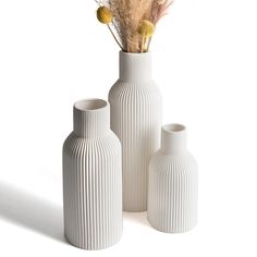 three white vases with dried plants in them on a white surface, one is empty