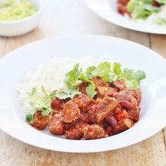 a white bowl filled with meat and rice on top of a wooden table next to another plate