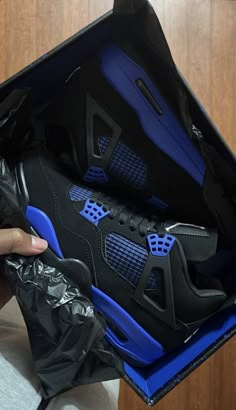 a person holding up a black and blue sneaker in a box with its lid open