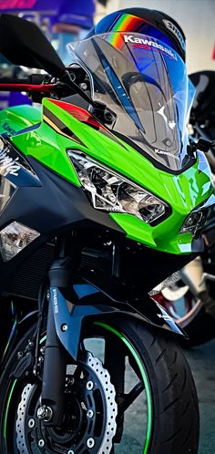 a green motorcycle parked in a parking lot next to other motorcycles with helmets on them