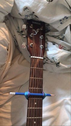 an acoustic guitar laying on top of a bed with white sheets and blue string attached to it