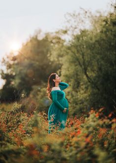 a pregnant woman in a blue dress standing in tall grass