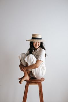 a woman sitting on top of a wooden stool wearing a white shirt and wide brimmed hat