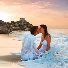 a man and woman sitting on the beach kissing