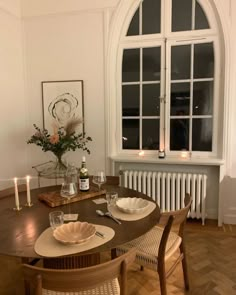 a wooden table with plates and glasses on it in front of a large arched window