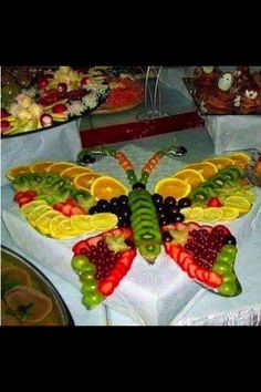 a butterfly made out of fruit on top of a white table cloth with other fruits and vegetables around it