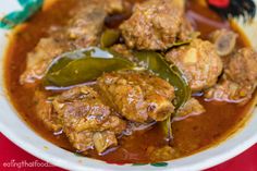 a white bowl filled with meat and vegetables covered in sauce on top of a red table