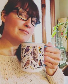 a woman wearing glasses is holding a coffee mug