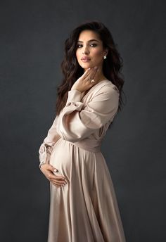 a pregnant woman posing for a photo in a long dress with her hands on her stomach