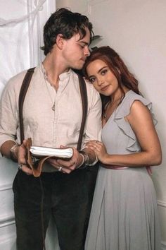 a man and woman standing next to each other in front of a white wall with curtains