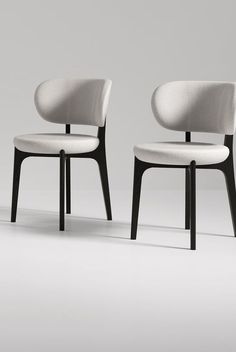 two white chairs sitting next to each other on top of a gray floor with black legs