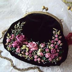 a black purse with pink flowers on it and a chain around the strap, sitting on a white lace tablecloth