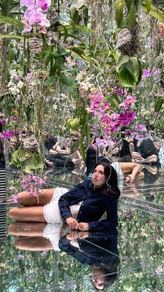 a woman laying on the ground surrounded by plants and flowers in a garden with water