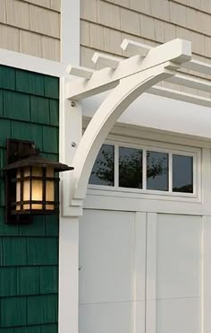 a green house with a white door and an arch over the garage door that has a light on it