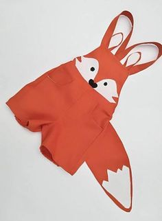 an orange apron with a fox design on the front and side, sitting on a white surface