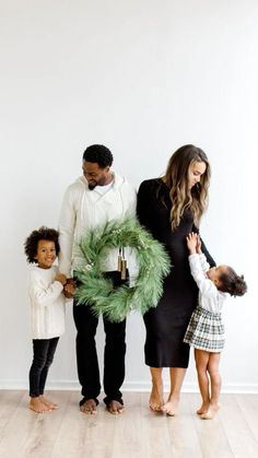 a family standing in front of a white wall holding a christmas wreath and two children