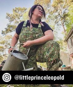 a woman in camouflage pants holding a bucket and looking up at the sky with her eyes closed