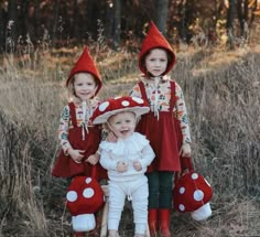 three children wearing red and white outfits standing in the grass with mushrooms on their heads