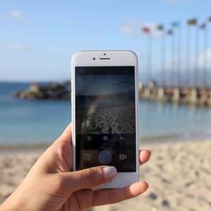 someone holding up their cell phone on the beach