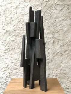 a black sculpture sitting on top of a wooden table in front of a white wall